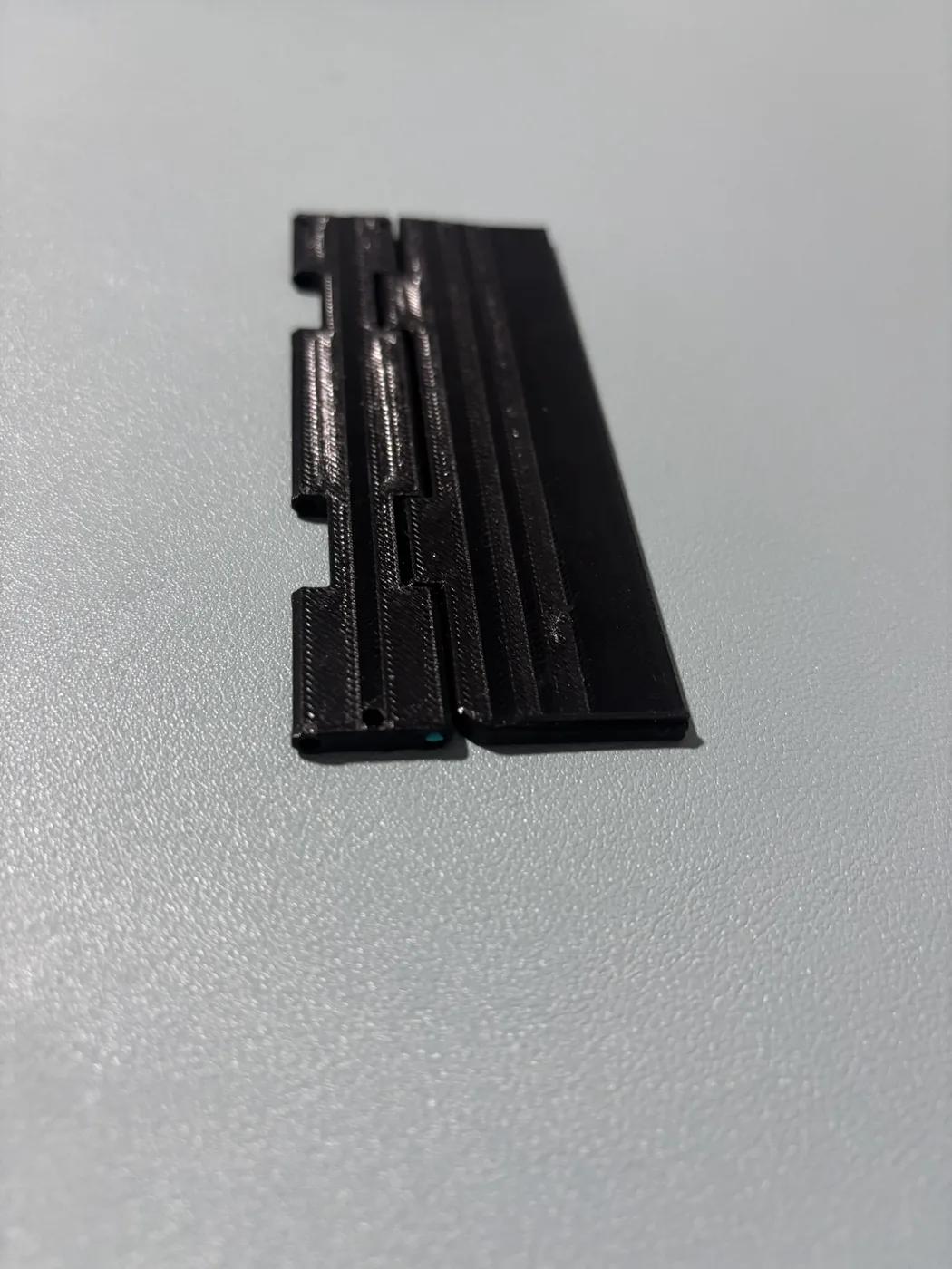Black printed hinge sample lying flat with a short cover-edge strip attached.
