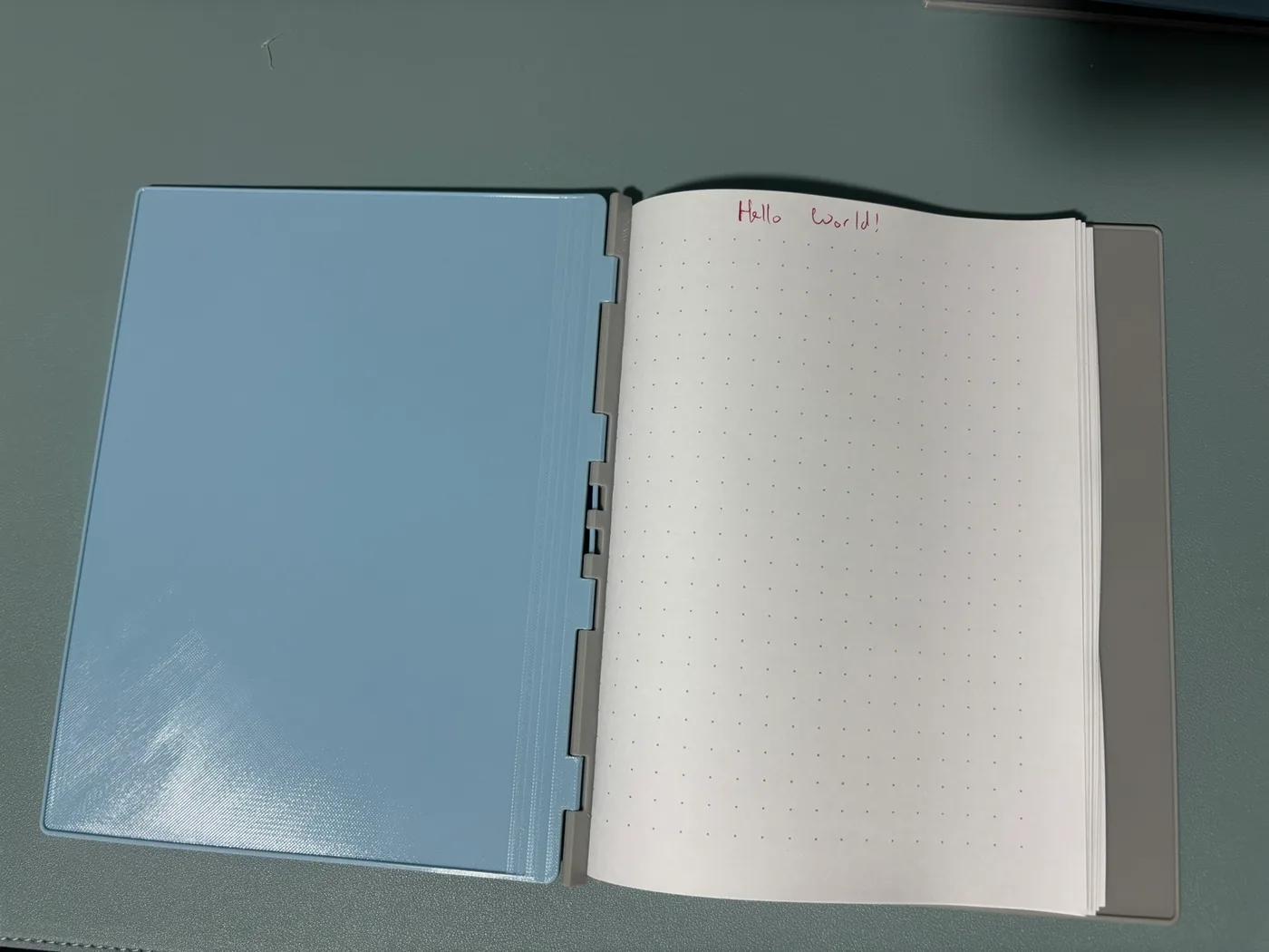 Open printed notebook in landscape orientation, with Hello world written across a page of dotted paper.